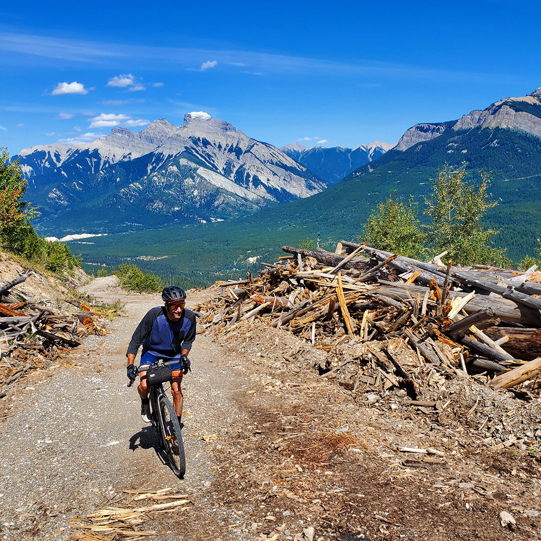 Person riding a bicycle on a mountain trail with scenic mountains in the background